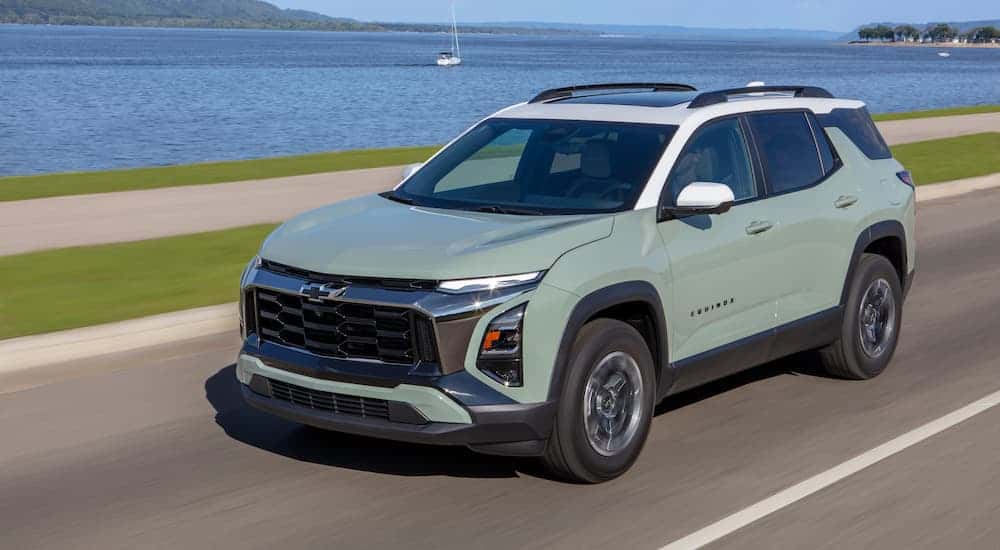 A green 2025 Chevy Equinox ACTIV driving near a lake.