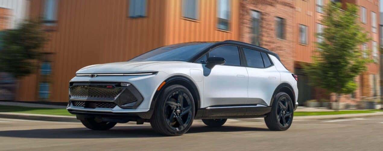 A white 2025 Chevy Equinox EV RS is shown driving on a city street.