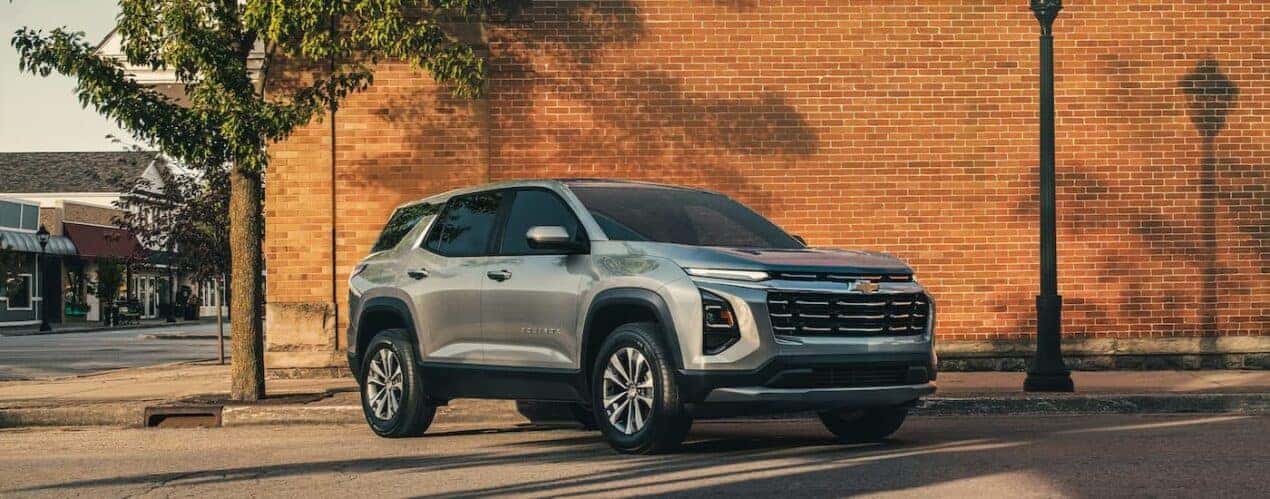 A silver 2025 Chevy Equinox LT is shown parked near a brick building.