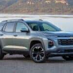 A grey 2025 Chevy Equinox LT parked on gravel with a lake view.
