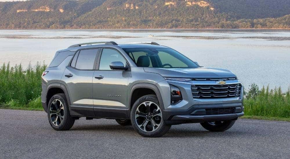 A grey 2025 Chevy Equinox LT parked on gravel with a lake view.