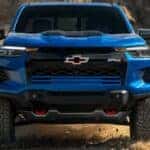 A blue 2025 Chevy Colorado ZR2 driving on a dusty dirt road.