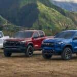 Three 2025 Chevy Colorado trucks for sale in Albany parked on dirt.