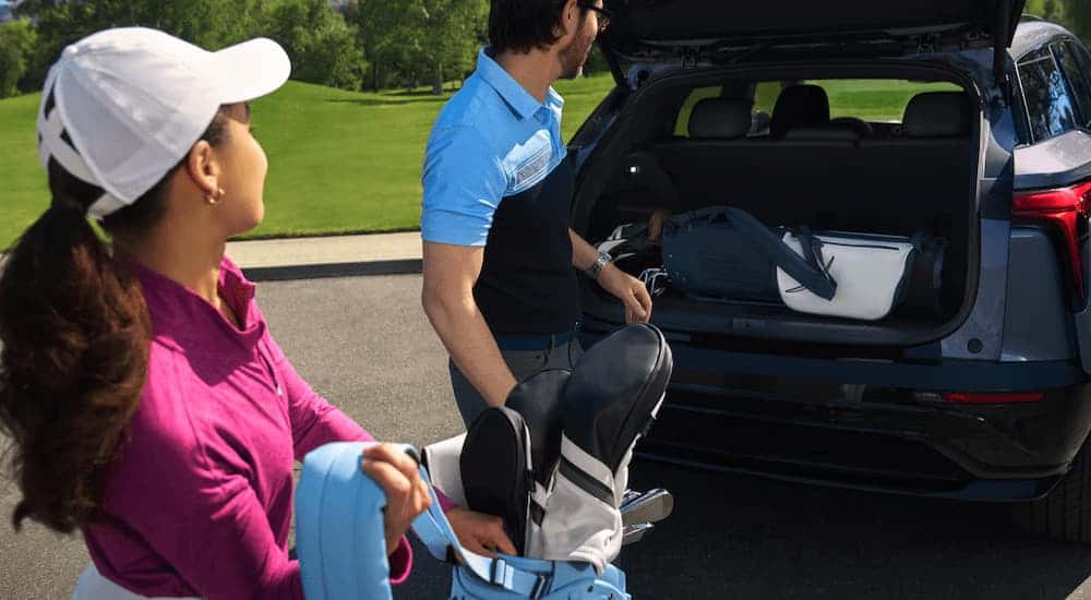 Two people putting golf gear in the back of a grey 2025 Chevy Blazer EV.
