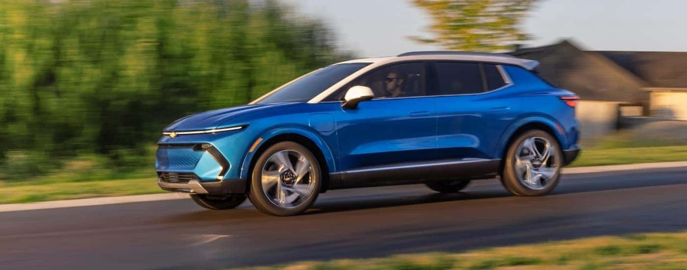 A blue 2025 Chevy Equinox EV 3LT driving past a house.