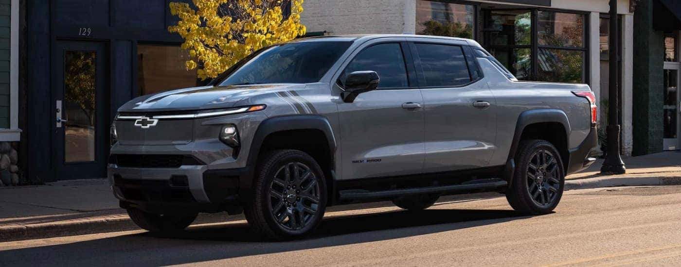 A grey 2025 Chevy Silverado EV LT parked in front of a shop.