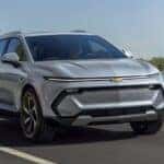 A silver 2025 Chevy Equinox EV for sale is driving on a highway.