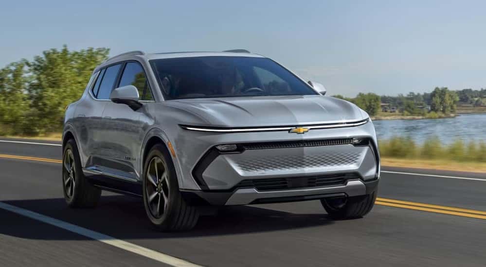 A silver 2025 Chevy Equinox EV for sale is driving on a highway.