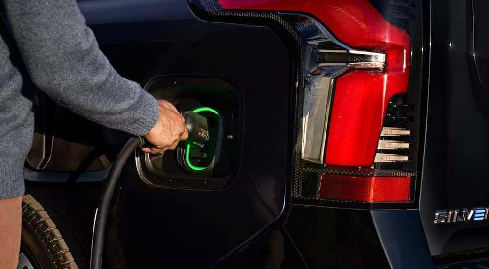 A person charging a black 2025 Chevy Silverado EV.