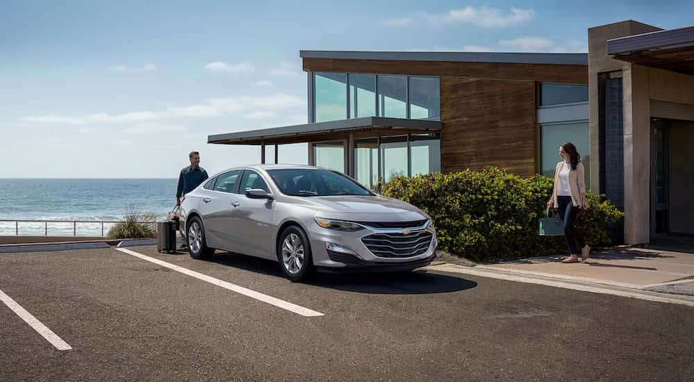 A silver 2025 Chevy Malibu parked near a modern house.