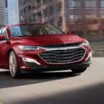 A red 2025 Chevy Malibu for sale near Latham driving in a city.