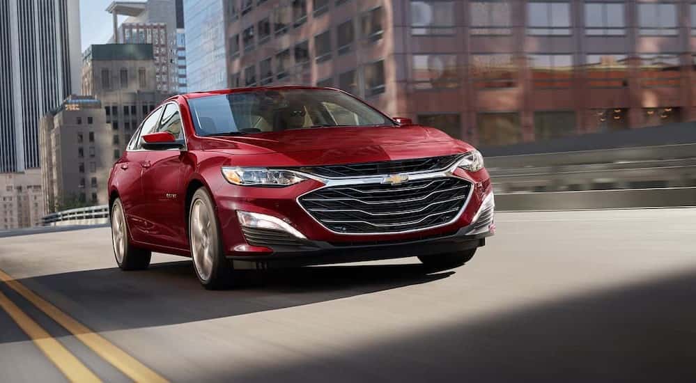 A red 2025 Chevy Malibu for sale near Latham driving in a city.