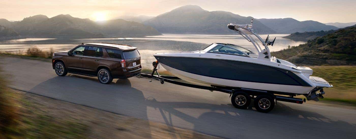 A brown 2022 Chevy Tahoe towing a boat near a lake.