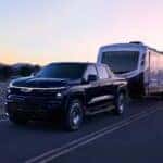 A black 2025 Chevy Silverado EV RST towing a trailer.