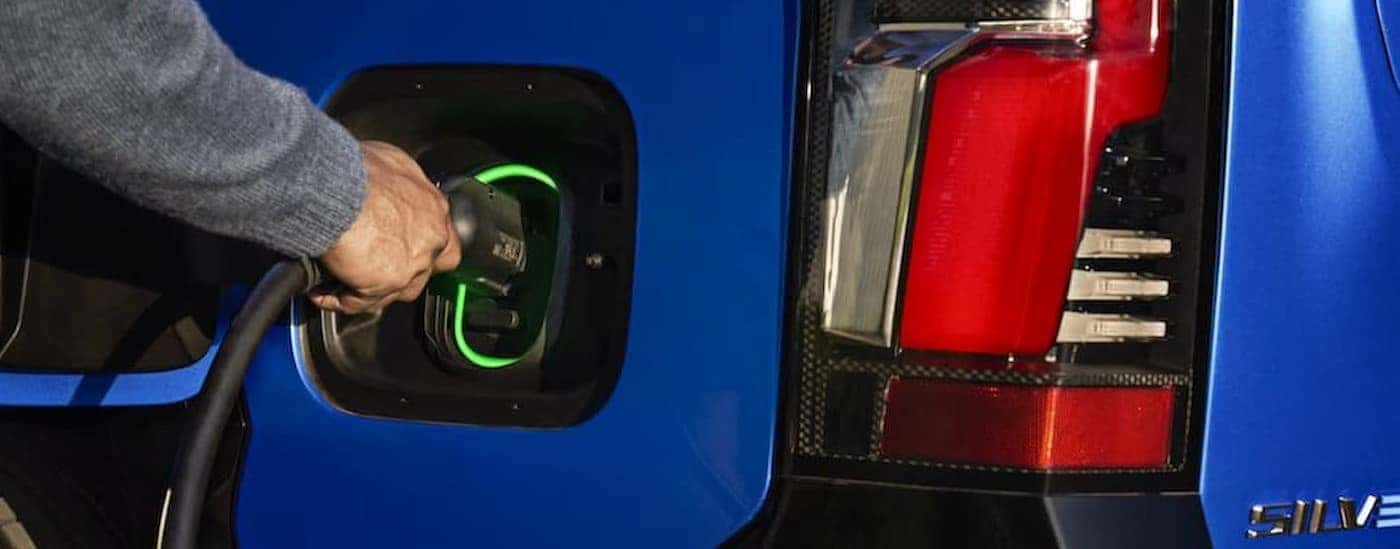 A person charging a blue 2025 Chevy Silverado EV.