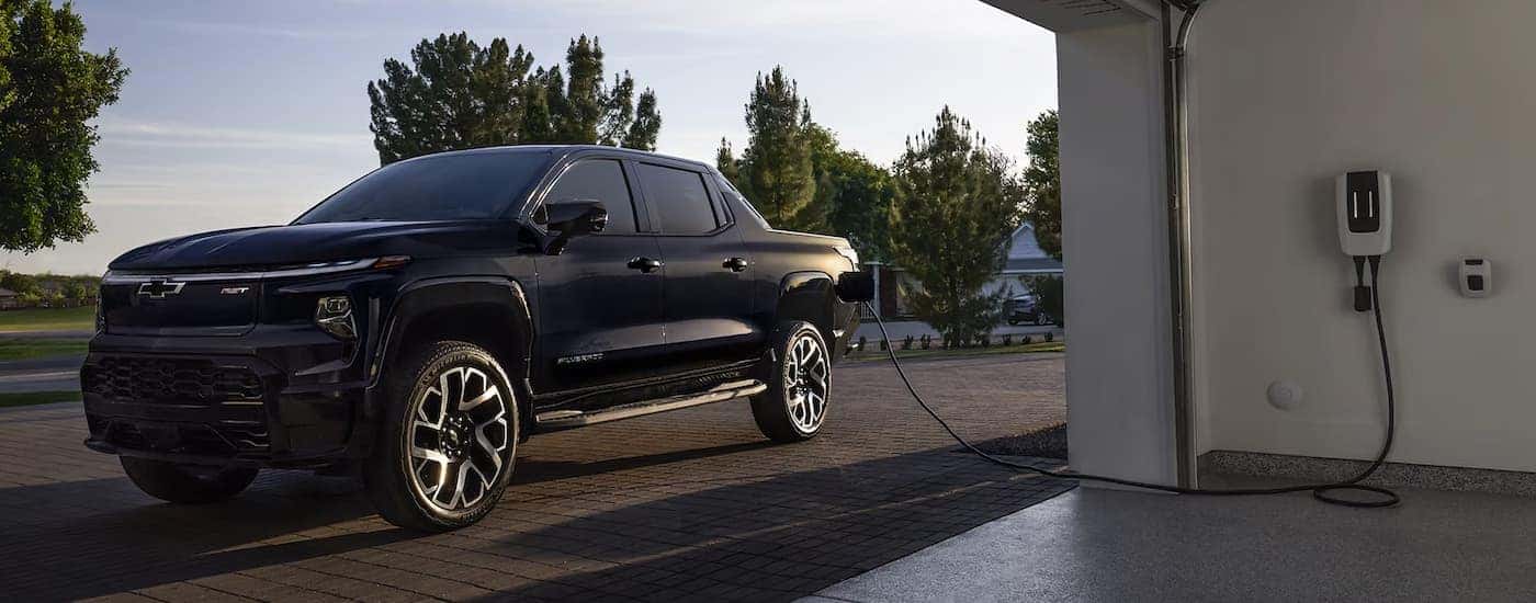 Black 2025 Chevy Silverado EV charging outside of a garage
