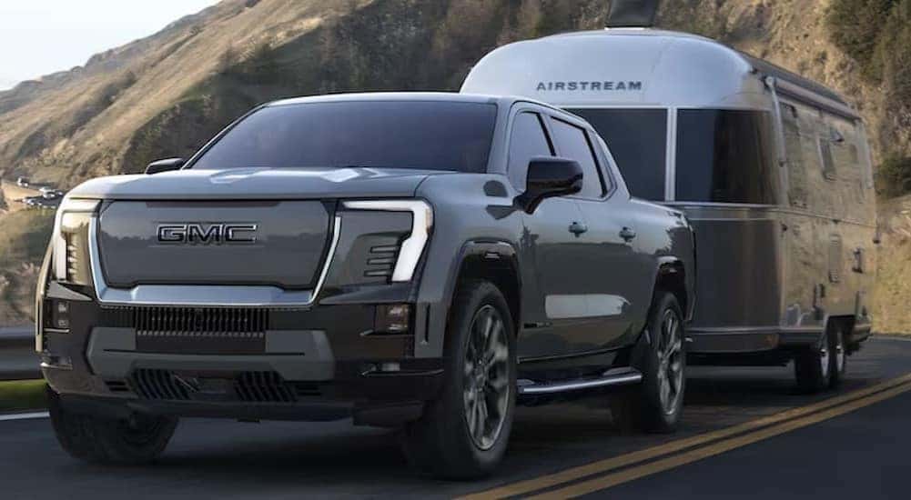 Black 2025 GMC Sierra EV towing an Airstream camper up a mountain road. 