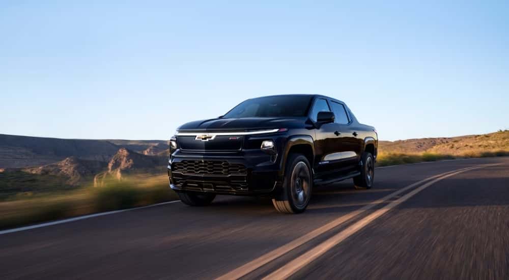 Black 2025 Chevy Silverado RST driving down open road.