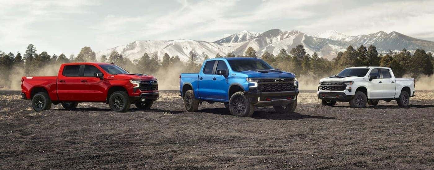 A red 2026 Chevy Silverado 1500 Z71, a blue 2026 Chevy Silverado 1500 ZR2 and a white 2026 Chevy Silverado 1500 High Country lined up. 
