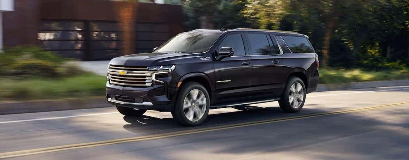 A blue 2023 Chevy Suburban High Country driving near houses.