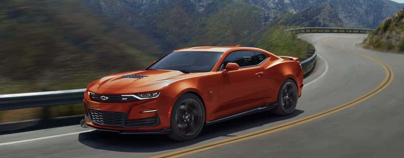 An orange 2024 Chevy Camaro driving to a used car dealer near Colonie.