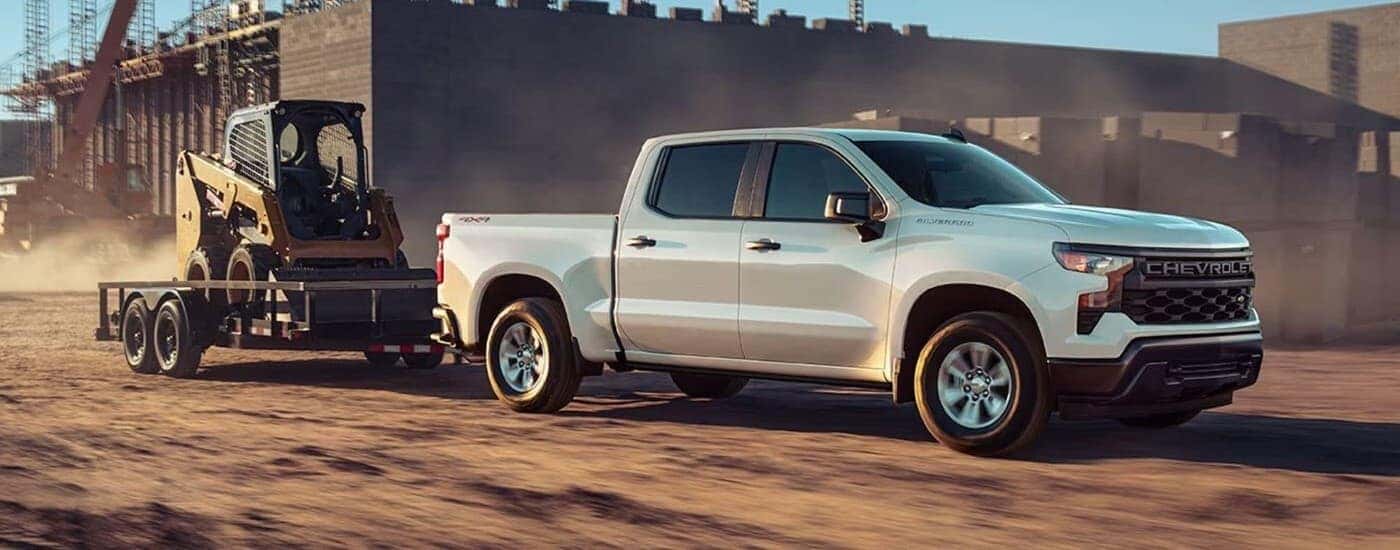 A white 2023 Chevy Silverado 1500 towing a trailer.