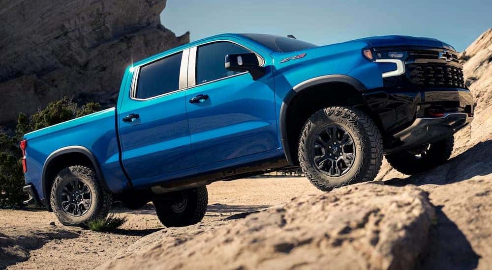 Side of a blue 2024 Chevy Silverado 1500 ZR2 driving off-road up a hill.