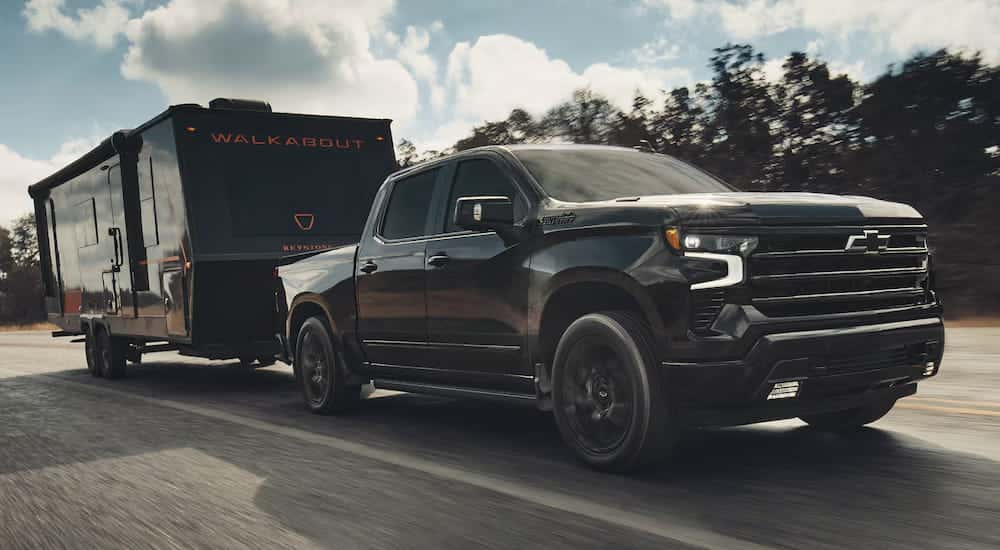 Black 2026 Chevy Silverado 1500 High Country towing a trailer down a road.