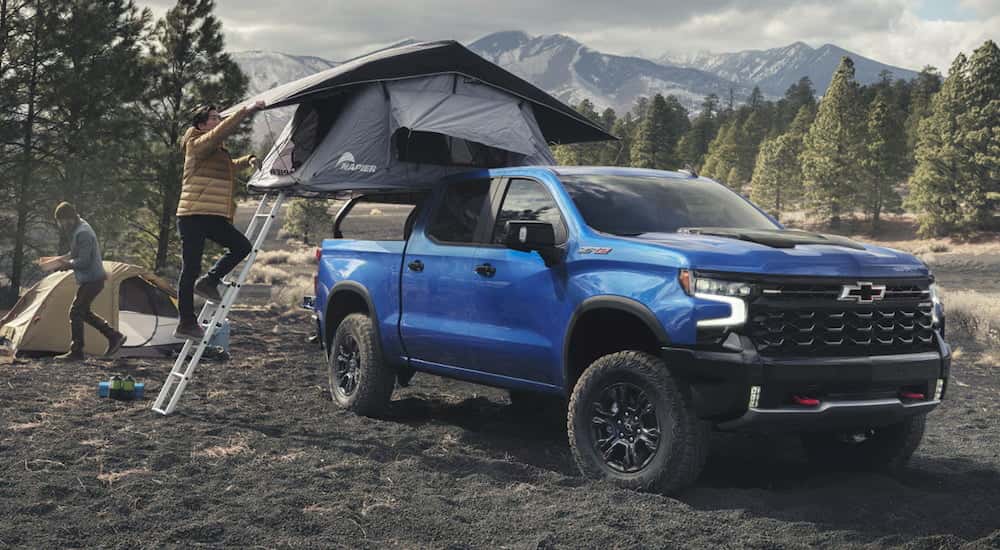 Person setting up a tent over the bed of a blue 2026 Chevy Silverado 1500.