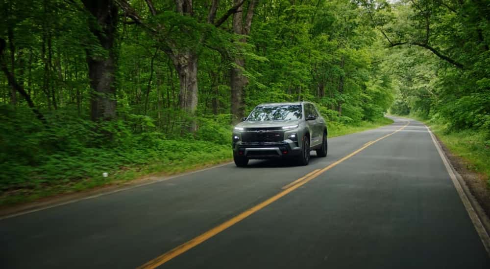 Black 2026 Chevy Traverse driving down a wooded road