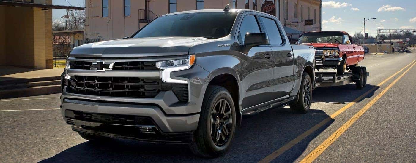 Grey 2026 Chevy Silverado 1500 RST towing a red car on a trailer