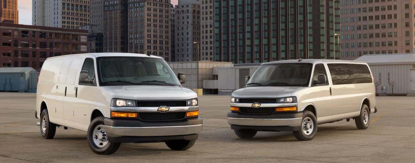 Two white 2026 Chevy Commercial Vans parked at a jobsite
