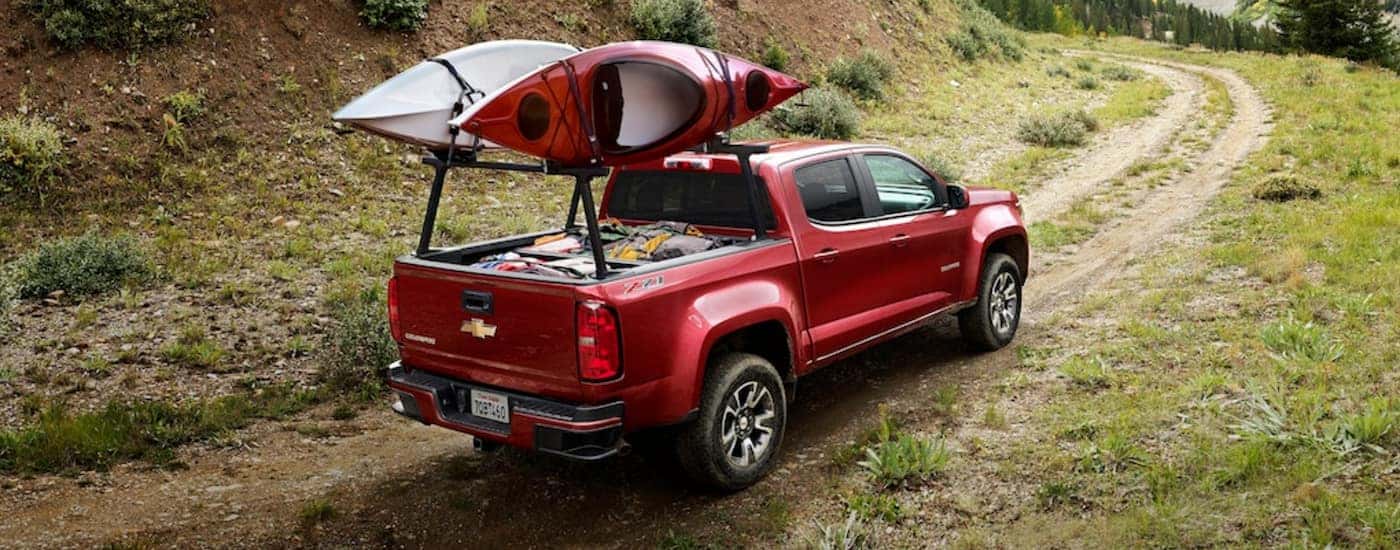 Red 2020 Chevy Colorado driving on a remote dirt trail with kayaks on the top.