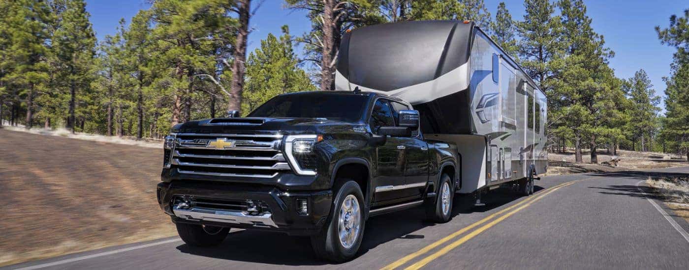 Black 2026 Chevy Silverado 2500 towing a camper down the road.