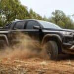 A black 2026 Chevy Colorado Trail Boss Midnight Edition driving on a dirt field.