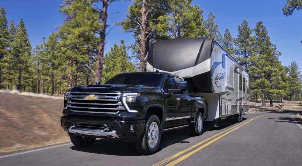 Black 2026 Chevy Silverado HD 2500 towing a camper on a paved road.