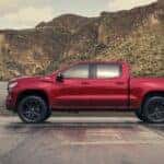 Side view of a red 2026 Chevy Silverado LD Crew Cab RST parked by docks and water.