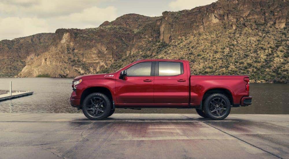 Side view of a red 2026 Chevy Silverado LD Crew Cab RST parked by docks and water.