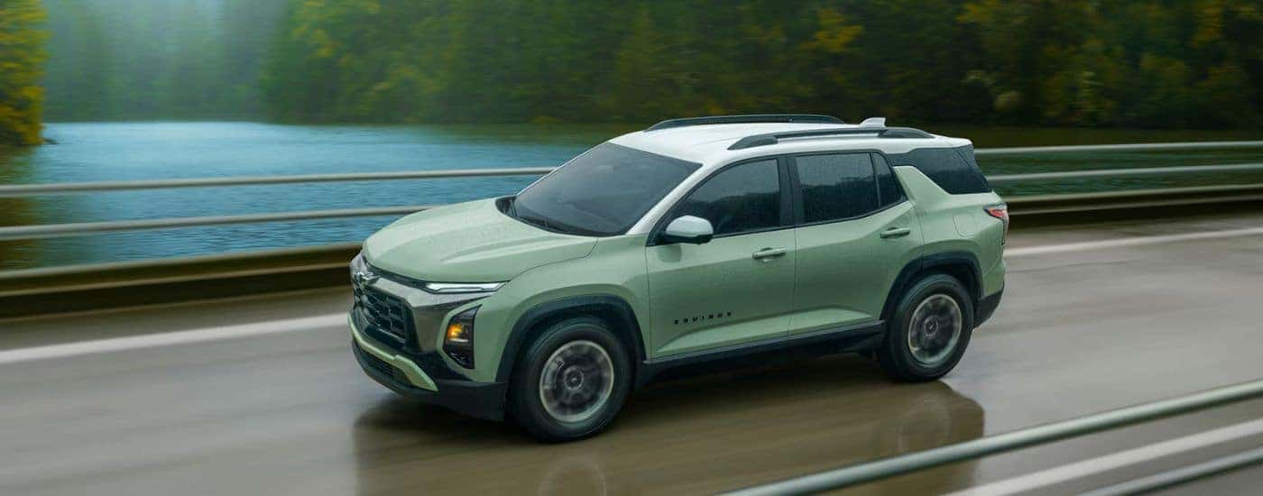 Green 2026 Chevy Equinox Activ driving on a paved road near a lake.