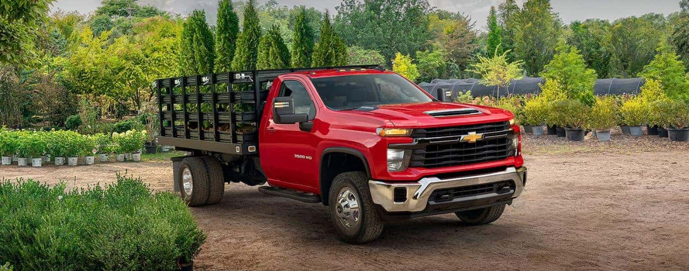 A red 2026 Chevy Silverado 3500 HD Chassis Cab hauling trees.
