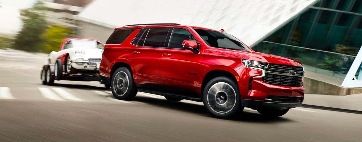 Red 2023 Chevy Tahoe towing a car on a paved road.