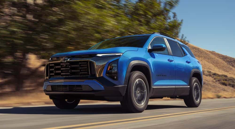 A blue 2027 Chevy Equinox driving by trees.
