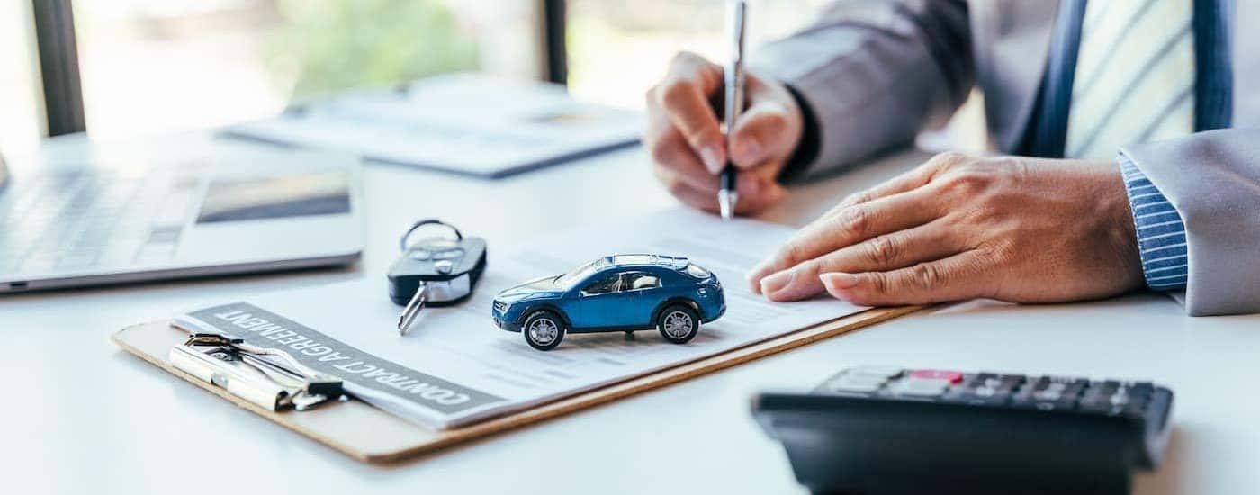 A person signing documents near a toy car and keys.