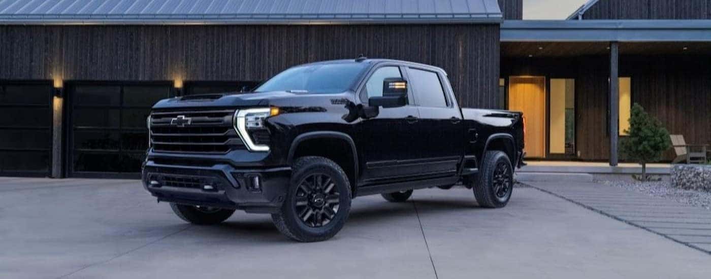 A black 2024 Chevy Silverado 2500 HD High Country parked near a garage.