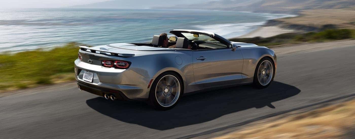 A silver 2021 Chevy Camaro Convertible is shown from the rear at an angle after leaving a dealer that has used cars for sale.