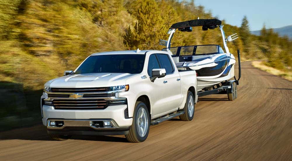 White 2021 Chevy Silverado 1500 diesel towing a boat on a dirt road.