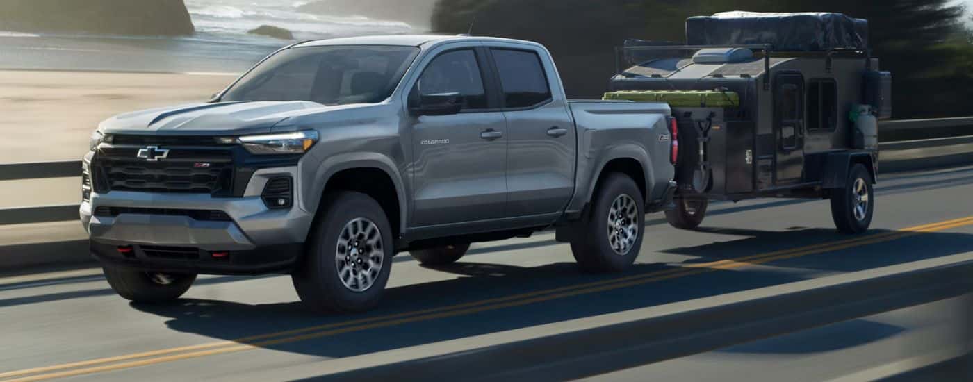 Grey 2027 Chevy Colorado Z71 towing a camper on a paved road.