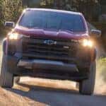 Front view of a red 2027 Chevy Colorado Trail Boss driving on a dirt road.