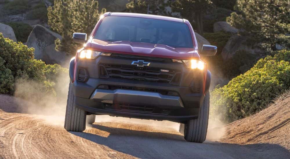Front view of a red 2027 Chevy Colorado Trail Boss driving on a dirt road.