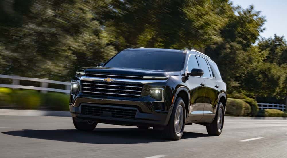 A black 2027 Chevy Traverse driving by a fence.